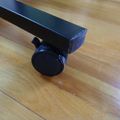 A black furniture leg with a wheel caster attached, sitting on a wooden floor