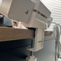 A beige desk clamp or vise attached to the edge of a wooden table surface