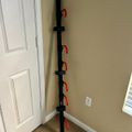 A black vertical pole with multiple red hooks or attachments mounted in the corner of a room with beige walls, white doors, and carpet flooring.