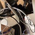 A desk setup with multiple white cables and cords connected to electronic devices, with a world map visible on the wall in the background