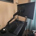 A computer workstation with a black ASUS monitor mounted on an adjustable arm above a laptop and keyboard on a dark desk