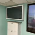 Interior room with mint green walls, white cabinet, wall-mounted TV, drop ceiling, and window showing outdoor view