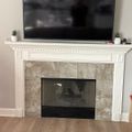 Living room with white fireplace mantel, stone surround, mounted flat screen TV above, and hardwood floors