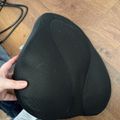A person holding a black mesh lumbar support cushion while sitting on a wooden floor