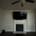 Living room with white fireplace, mounted TV above mantel, built-in white cabinets on either side, ceiling fan, and dark hardwood floors