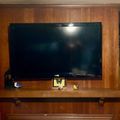 Large flat-screen TV mounted on wooden wall unit with built-in shelving and decorative items on the mantel below