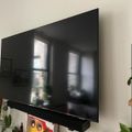 Large flat screen TV mounted on white wall with reflective black screen showing room's windows and interior