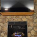 Stone fireplace with mounted flat screen TV above wooden mantel, gas flames visible in firebox