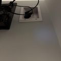 Wall outlet with black cables and device plugged in on white wall surface