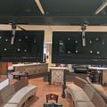 Interior of a recreational room with two large ceiling-mounted TVs, comfortable seating arrangements, and what appears to be a bar or counter area in the background