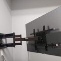 A flat screen TV mounted on a white wall with an adjustable black wall mount bracket that extends outward from the wall