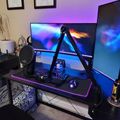 A modern gaming setup with dual monitors, RGB lighting, microphone arm, and gaming chair in a home office with certificates on the wall