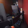 A cluttered desk setup with multiple computer monitors, keyboards, and electronic devices in a room with red and wood-paneled walls