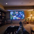 Person relaxing in basement entertainment room watching sports on large wall-mounted TV with feet up on ottoman