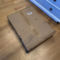 A damaged cardboard package lying on a wooden floor next to blue furniture with drawers