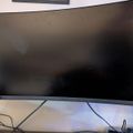 A large computer monitor with a dark screen sitting on a desk with cables and other electronic devices visible below it