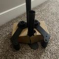 A black metal umbrella stand base with two cylindrical holders sitting on beige carpet next to a white wall