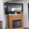 Living room with wooden fireplace mantel, mounted flat screen TV above, and hardwood floors with area rug