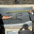 Two people measuring and installing a TV wall mount bracket on a kitchen wall with stone tile backsplash