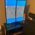 A dual monitor computer setup displaying trading charts and patterns, with a gaming keyboard, black office chair, and desk in a home office environment