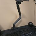 A computer workstation with a monitor on an adjustable arm mount, black keyboard, and mouse on a dark desk surface