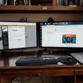 A dual monitor computer setup on a wooden desk with keyboard, mouse, and laptop, showing web browsers open on both screens