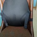 A gray lumbar support cushion with straps attached to a brown upholstered chair with wooden arms