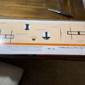 A packaged TV wall mount bracket with installation diagrams and instructions visible on the box, placed on a wooden surface with a knife nearby