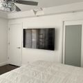 Modern bedroom with white bedding, wall-mounted TV, ceiling fan with crystal light fixture, and white doors leading to closet and bathroom