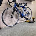 Blue road bike with aerobars mounted on indoor trainer in garage with tools on floor
