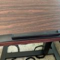 A laptop computer sitting on a wooden desk surface with a patterned rug visible underneath