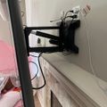 A black adjustable TV wall mount attached to a white wall above a white wooden cabinet, with various cables and cords visible