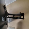 A black TV wall mount bracket extended from a beige wall with a white cylindrical object below it