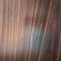 Wood grain surface with brown and reddish tones and a blue-green stain or discoloration in the center