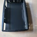 Black plastic electronic device case or housing with cutouts for buttons and camera, lying on a light colored surface