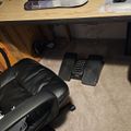 A home office workspace with a wooden desk, black office chair, keyboard, mouse, and foot rest on carpeted floor