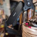 Black adjustable monitor arm mounted on a desk with office supplies in a wicker basket