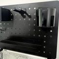 Black metal pegboard organizer with hooks and cylindrical holders mounted on adjustable legs