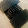 A compact black mechanical keyboard with dark keycaps displayed in an open protective case with ribbed texture on a wooden surface