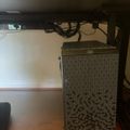 A computer tower with geometric patterned case sits under a dark wooden desk, with cables and a monitor visible above