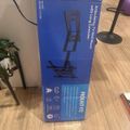 Blue product box for an articulating TV wall mount with long extension arm, sitting on wooden floor next to furniture