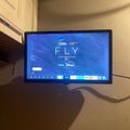 Computer monitor displaying a streaming service interface for a National Geographic documentary called "FLY" with Hulu and Disney+ logos, sitting on a desk in a room with white cabinets