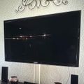 Wall-mounted flat screen TV with decorative metal scrollwork above it and speakers on a dark shelf below