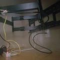 Desk setup with monitor arm mount and various cables connected to devices on a wooden surface