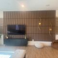 Modern living room with wooden slat accent wall, wall-mounted TV, dark blue media console, and contemporary furniture on hardwood floors