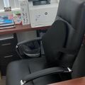Office workspace with black leather chair, wooden desk, HP printer, and various papers and documents