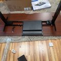 A desk setup showing an HP laptop docking station mounted under a wooden desk surface, with HP product boxes and packaging materials visible on top of the desk and floor