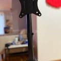 Black adjustable monitor stand with mounting bracket on desk in office setting