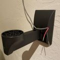 Black wall-mounted hair dryer holder with cord management attached to white textured wall