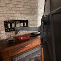 A TV wall mount bracket extends from a brick wall above a wooden entertainment center with fireplace insert
